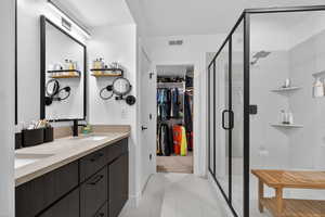 Full bath with double vanity, a spacious closet, a shower stall, and light tile patterned flooring