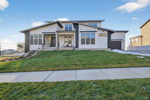 View of front of property with a porch, a front yard, and an attached garage