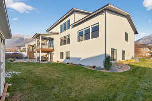 Back of house featuring a mountain view, stucco siding, and a lawn