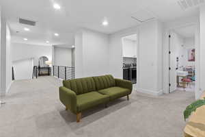 Sitting room featuring light colored carpet, washing machine and dryer, recessed lighting, and an upstairs landing
