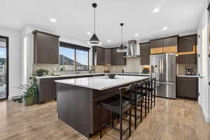 Kitchen with dark brown cabinets, a breakfast bar, stainless steel fridge, backsplash, and recessed lighting