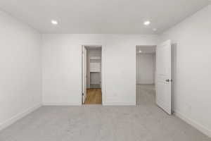 Unfurnished bedroom with a walk in closet, light carpet, and recessed lighting
