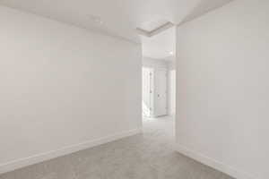 Carpeted spare room featuring attic access and baseboards