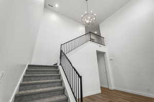 Stairway featuring a towering ceiling, wood finished floors, a chandelier, and recessed lighting