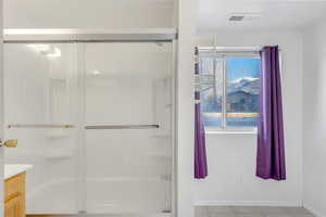 Full bath with combined bath / shower with glass door, vanity, and light tile patterned floors