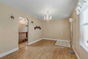 Spare room featuring a chandelier, light wood-style flooring, and arched walkways