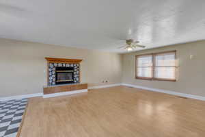 Unfurnished living room with a fireplace, light floors, and ceiling fan