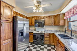 Kitchen featuring dark floors, brown cabinetry, stainless steel refrigerator with ice dispenser, black microwave, and light stone countertops