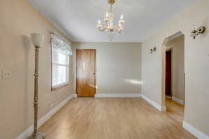 Unfurnished dining area with a chandelier, light wood finished floors, and arched walkways