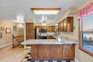 Kitchen featuring brown cabinets, light stone counters, a peninsula, and black microwave