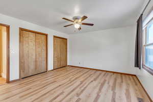 Unfurnished bedroom featuring two closets, light wood finished floors, and ceiling fan