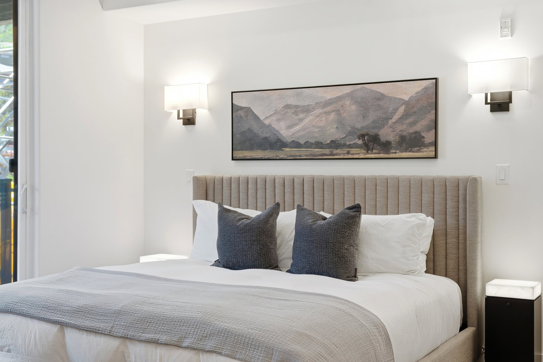 Bedroom featuring a channeled upholstered headboard, white walls, and dual wall-mounted sconces