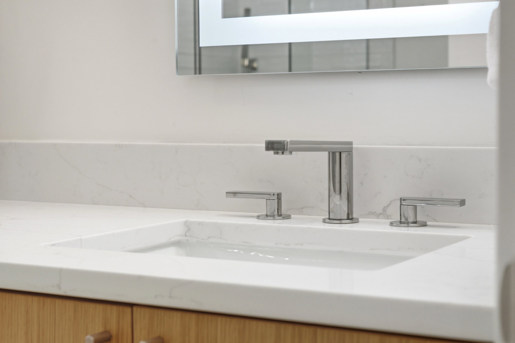 Modern vanity featuring an integrated rectangular sink, widespread chrome faucet, and light wood-finish cabinetry