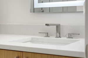 Modern vanity featuring an integrated rectangular sink, widespread chrome faucet, and light wood-finish cabinetry