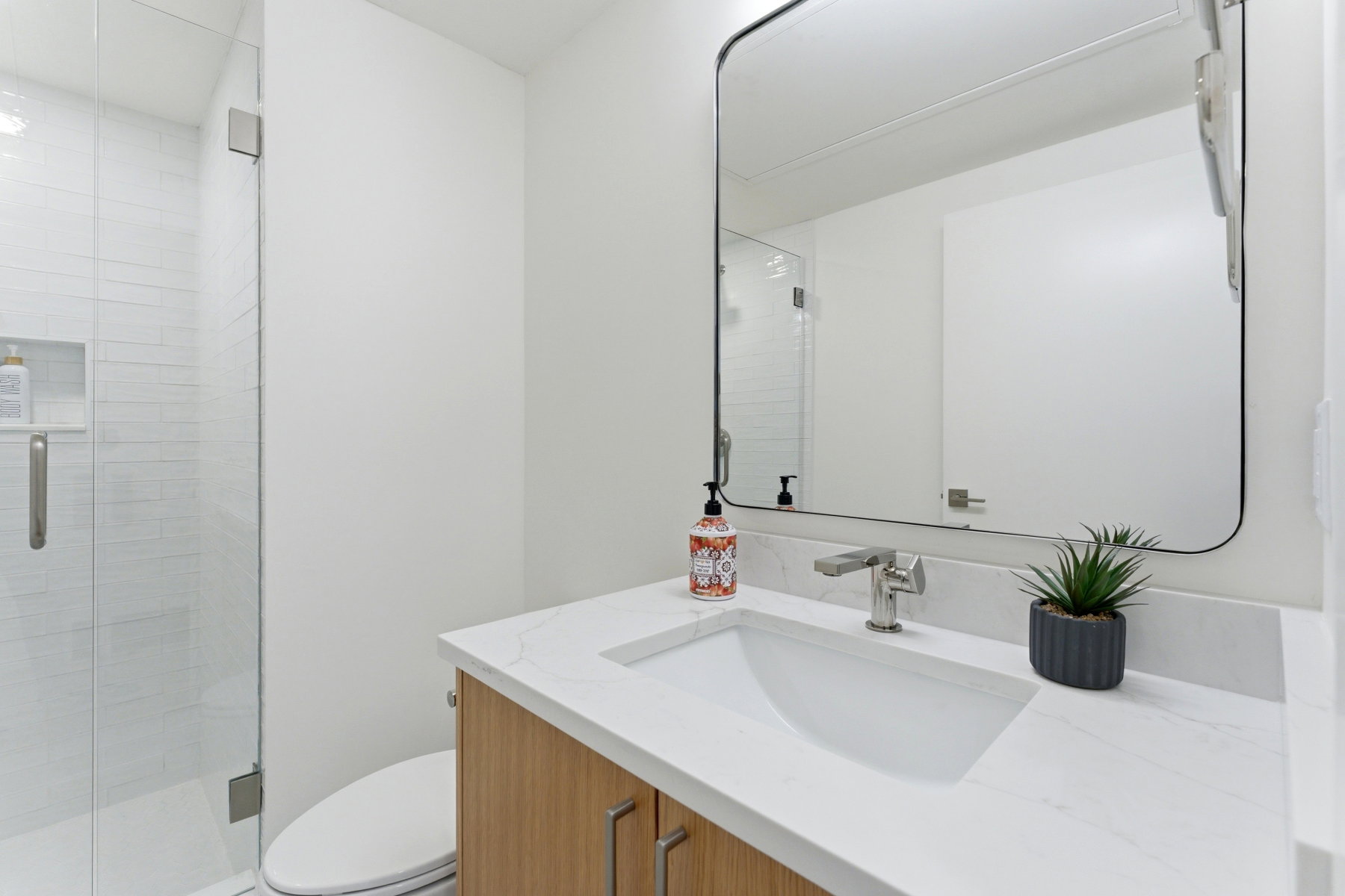 Contemporary bathroom featuring a light wood-finish vanity with an integrated rectangular sink, a light-colored countertop, and a sleek rectangular mirror
