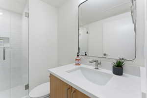 Contemporary bathroom featuring a light wood-finish vanity with an integrated rectangular sink, a light-colored countertop, and a sleek rectangular mirror