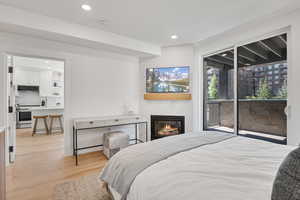 Bedroom with light wood finished floors, access to exterior, a large fireplace, and recessed lighting