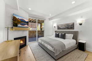 Bedroom featuring a stone-clad fireplace with a natural wood mantel, light wood-finish flooring, recessed lighting, and direct access to an outdoor patio through sliding glass doors