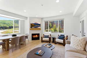Open-concept living space with light wood-finish flooring, a contemporary fireplace with a stone surround and wood mantel, large windows, and recessed lighting
