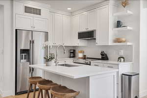 Kitchen featuring open shelves, stainless steel appliances, a kitchen breakfast bar, white cabinetry, and a center island with sink