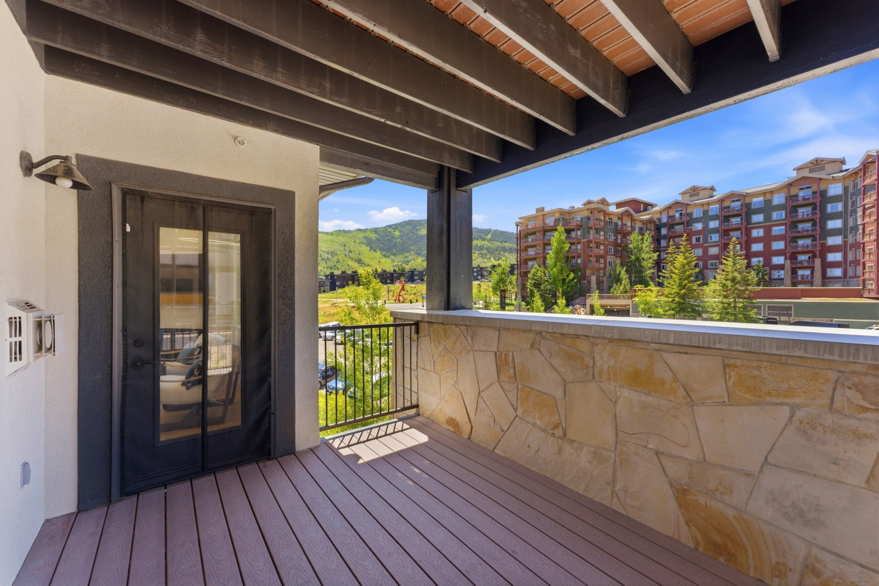 Spacious outdoor balcony featuring composite decking, a stone-clad half-wall, and a black metal railing