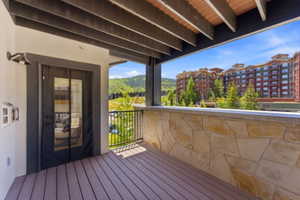 Spacious outdoor balcony featuring composite decking, a stone-clad half-wall, and a black metal railing
