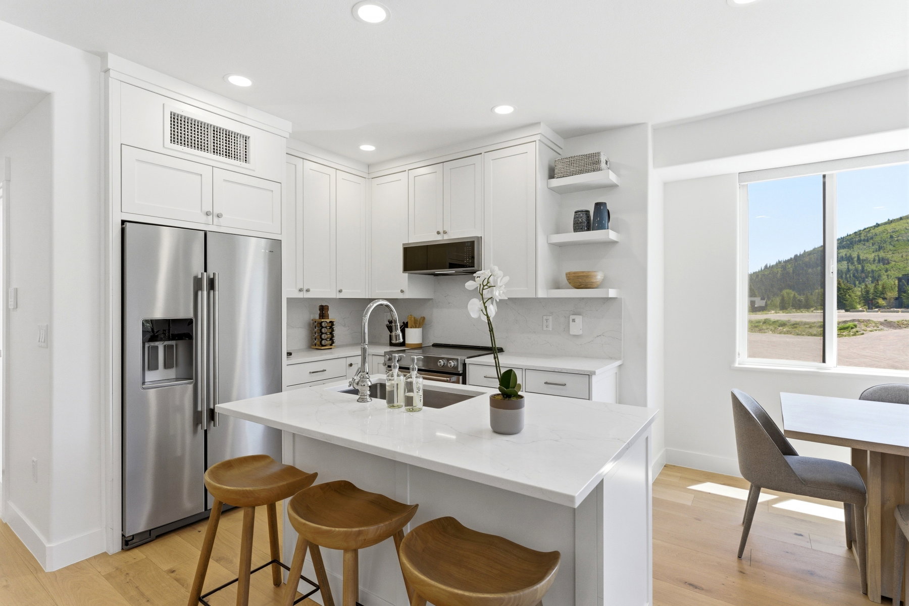 Modern kitchen featuring white shaker cabinetry, stainless steel appliances, a center island with seating, pendant lighting, and wood-finish flooring