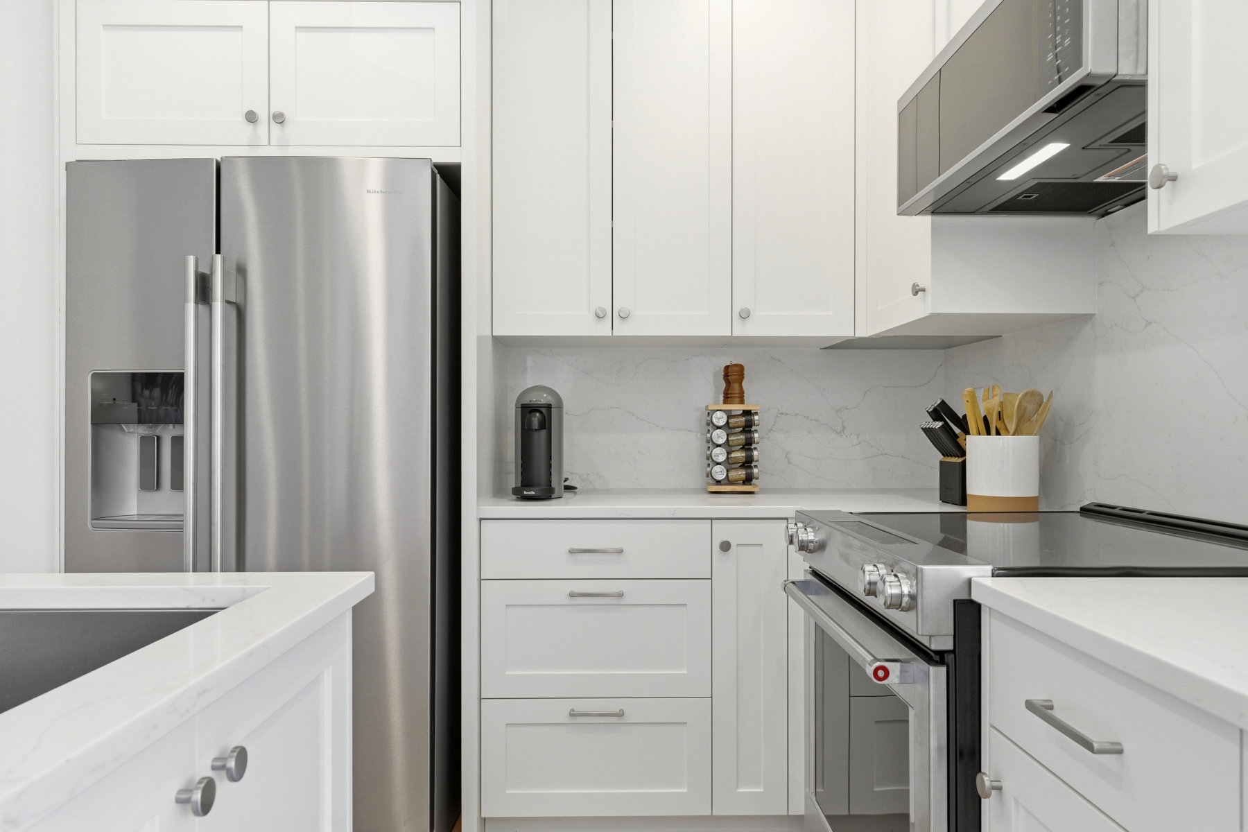 Contemporary kitchen featuring white shaker cabinetry, stainless steel appliances, solid surface countertops, a built-in range, and a matching range hood