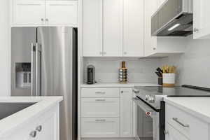 Contemporary kitchen featuring white shaker cabinetry, stainless steel appliances, solid surface countertops, a built-in range, and a matching range hood