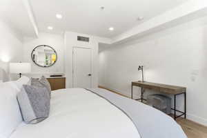 Recessed lighting illuminating the white walls, wood-finish flooring, built-in shelving with wood cabinetry, white door with black hardware, and a circular wall mirror with black framing