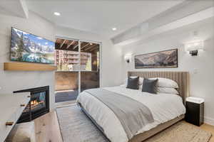 Bedroom with a tiled fireplace, light wood-style flooring, access to exterior, and recessed lighting