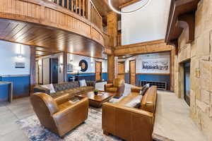 Spacious common area featuring a stone accent wall with fireplace, wood-paneled ceilings, and tile flooring