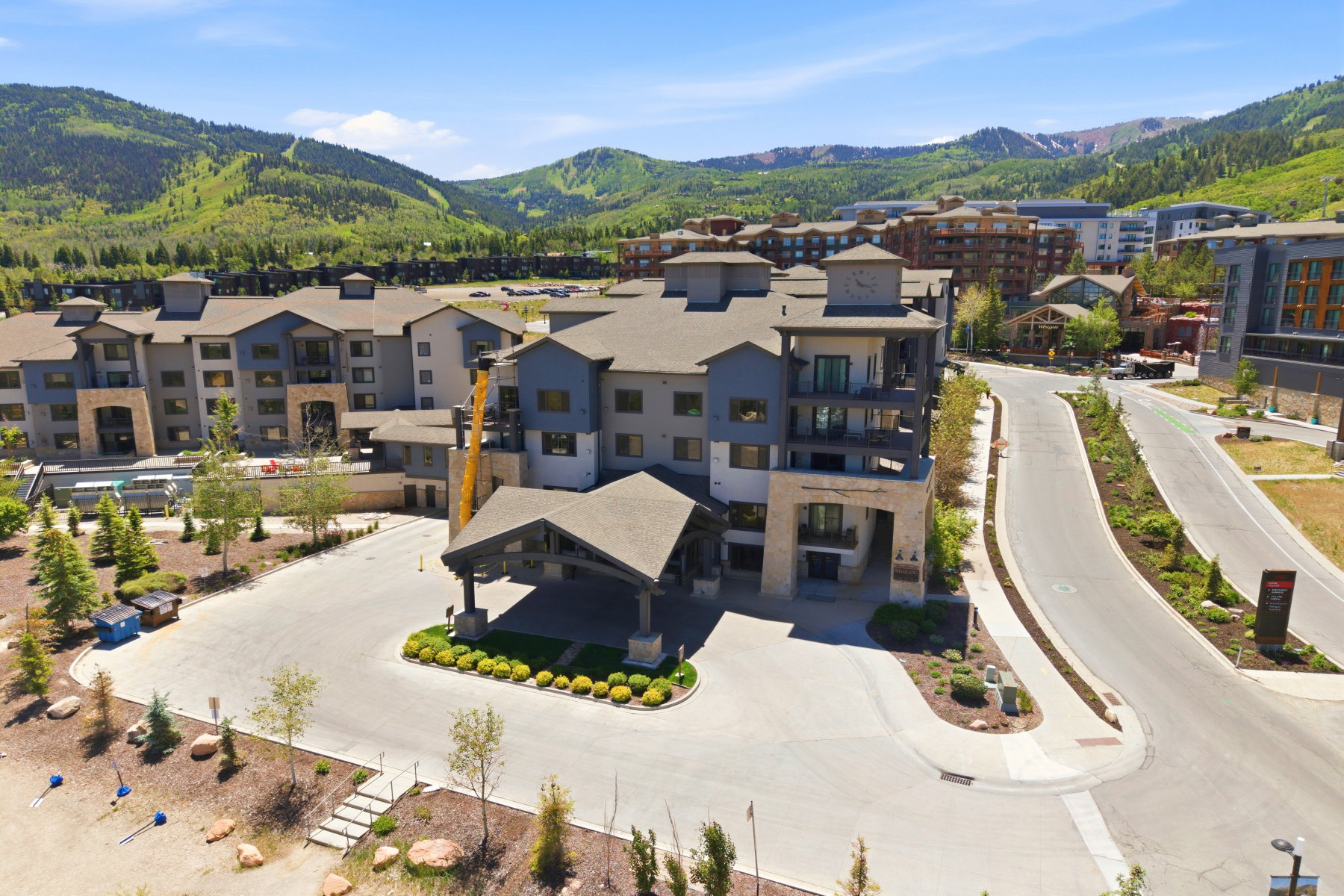 Contemporary multi-story building featuring a porte-cochère entrance, multiple balconies, a visible swimming pool, and mountainous terrain