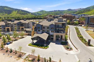 Contemporary multi-story building featuring a porte-cochère entrance, multiple balconies, a visible swimming pool, and mountainous terrain