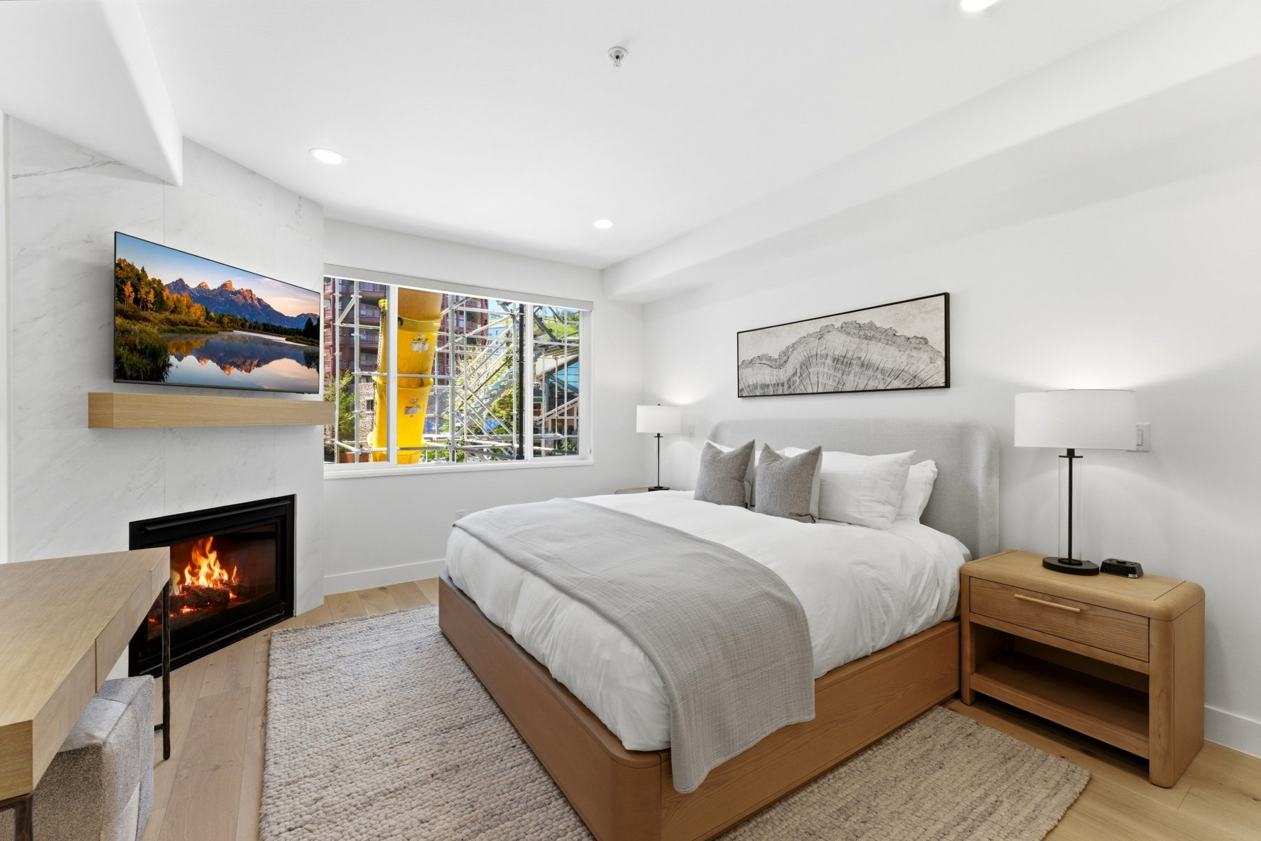 Contemporary bedroom featuring a built-in fireplace with a natural wood mantel, light wood-finish flooring, and a large window with roller shades