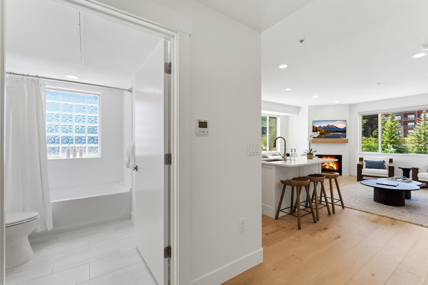 Open-concept living space with light wood-finish flooring, recessed lighting, and a white fireplace feature