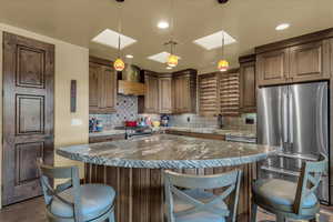 Kitchen with appliances with stainless steel finishes, a center island, decorative light fixtures, backsplash, and dark stone countertops