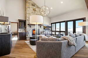 Living room featuring light wood-style flooring, a stone fireplace, high vaulted ceiling, and recessed lighting