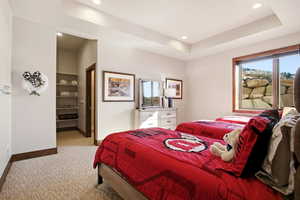 Bedroom with light colored carpet, a tray ceiling, multiple windows, and recessed lighting