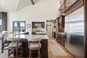 Kitchen with built in appliances, dark brown cabinets, light stone counters, recessed lighting, and high vaulted ceiling