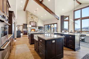 Kitchen featuring light stone counters, dark brown cabinetry, open floor plan, stainless steel appliances, and high vaulted ceiling