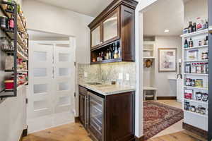 Kitchen with dark brown cabinetry, open shelves, beverage cooler, light stone counters, and tasteful backsplash