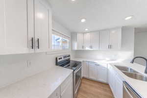 Kitchen featuring stainless steel appliances, white cabinets, recessed lighting, light wood finished floors, and light stone countertops