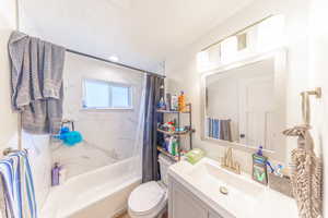 Full bathroom featuring vanity, shower / bathtub combination with curtain, and a textured ceiling