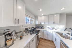 Kitchen featuring stainless steel appliances, light stone countertops, white cabinetry, light wood finished floors, and recessed lighting