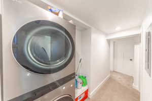 Laundry area featuring carpet flooring, stacked washer and clothes dryer, electric panel, and recessed lighting
