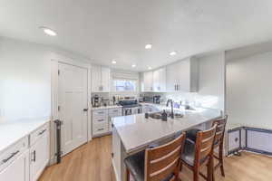 Kitchen with white cabinets, stainless steel electric stove, a kitchen bar, light stone countertops, and a peninsula