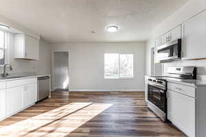 Kitchen with stainless steel appliances, light countertops, white cabinets, a textured ceiling, and wood finished floors