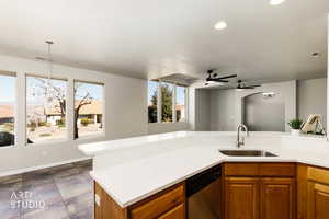 Kitchen with brown cabinetry, a chandelier, stainless steel dishwasher, a ceiling fan, and light stone countertops