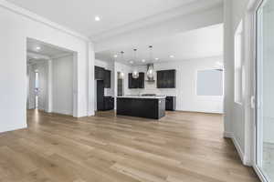 Kitchen featuring dark cabinets, light countertops, decorative backsplash, a center island with sink, and decorative light fixtures